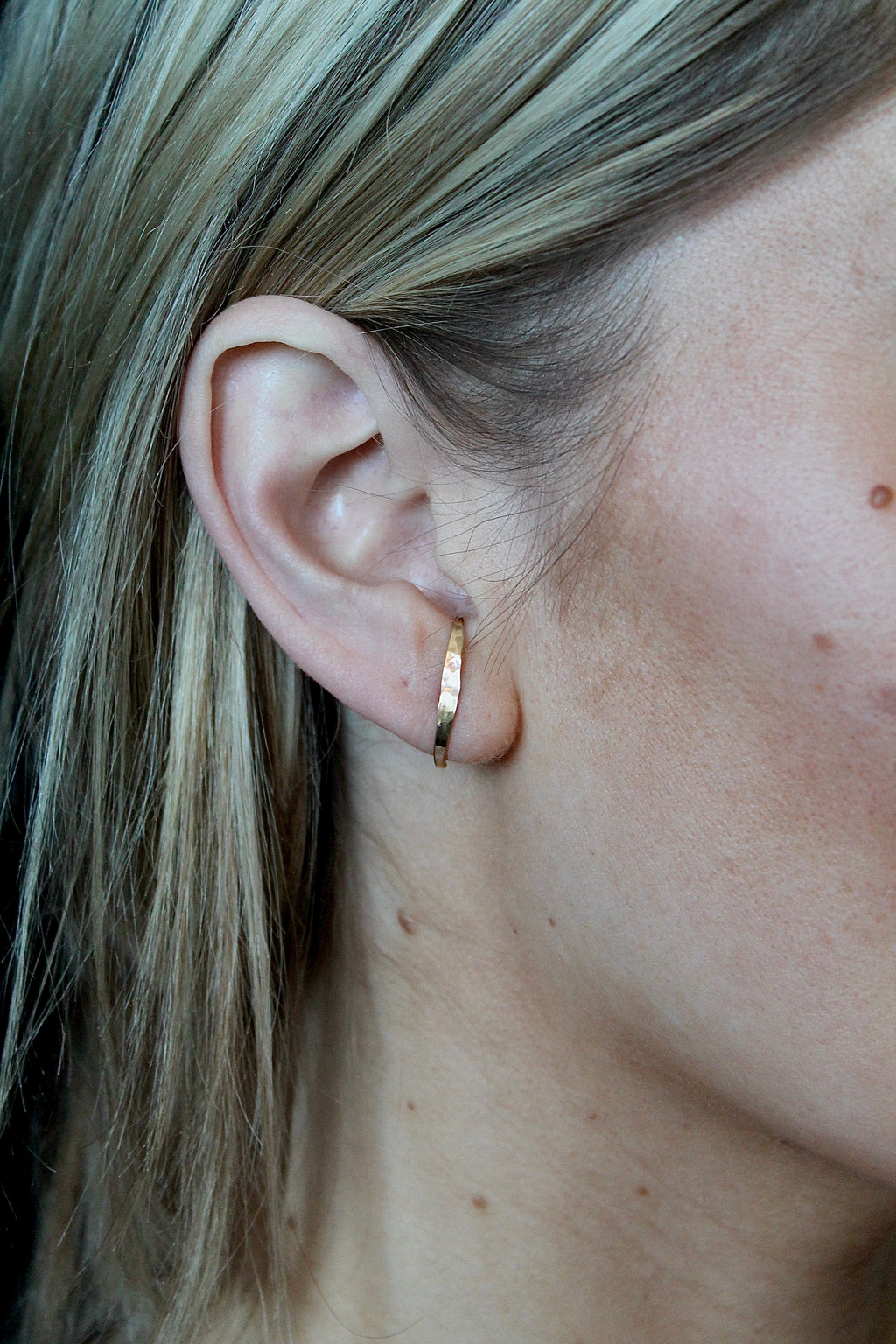 Close-up of a person wearing a gold hoop earring with blonde hair.