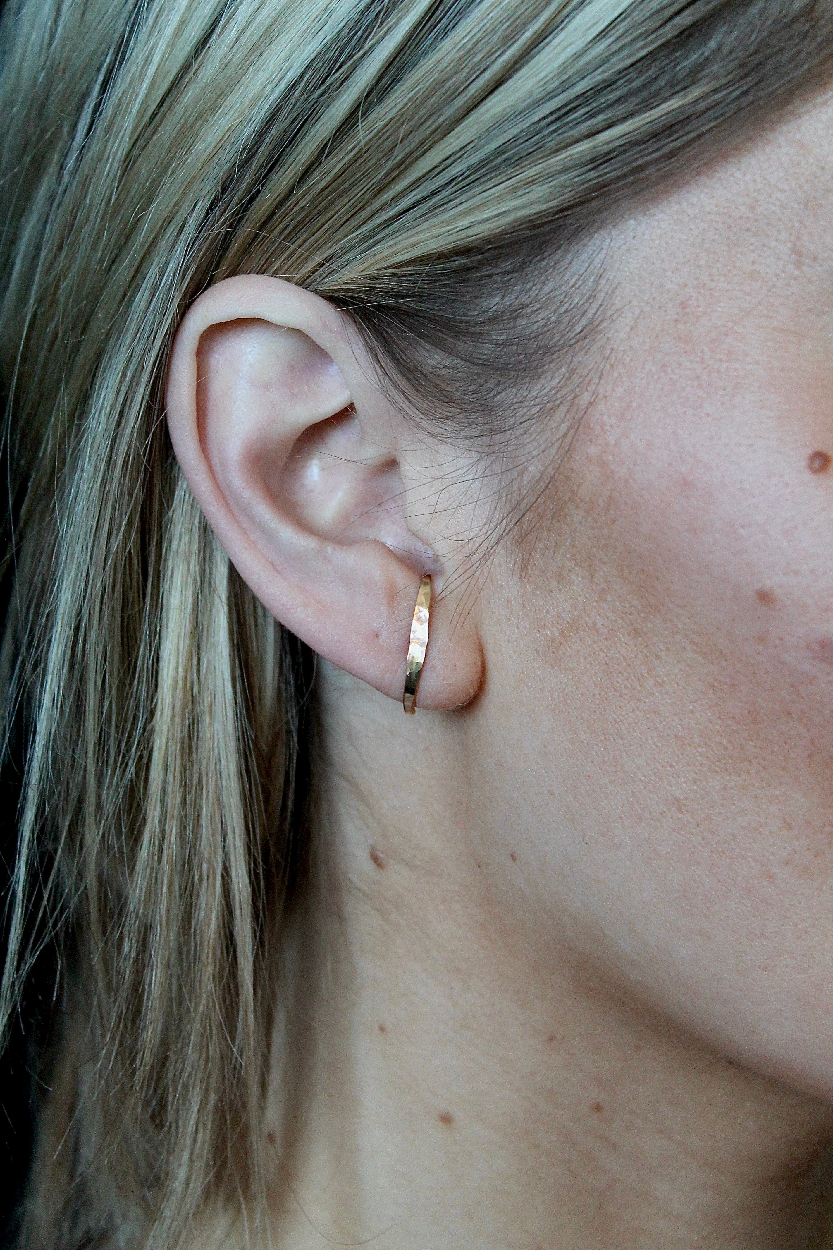 Close-up of a person wearing a gold hoop earring with blonde hair.