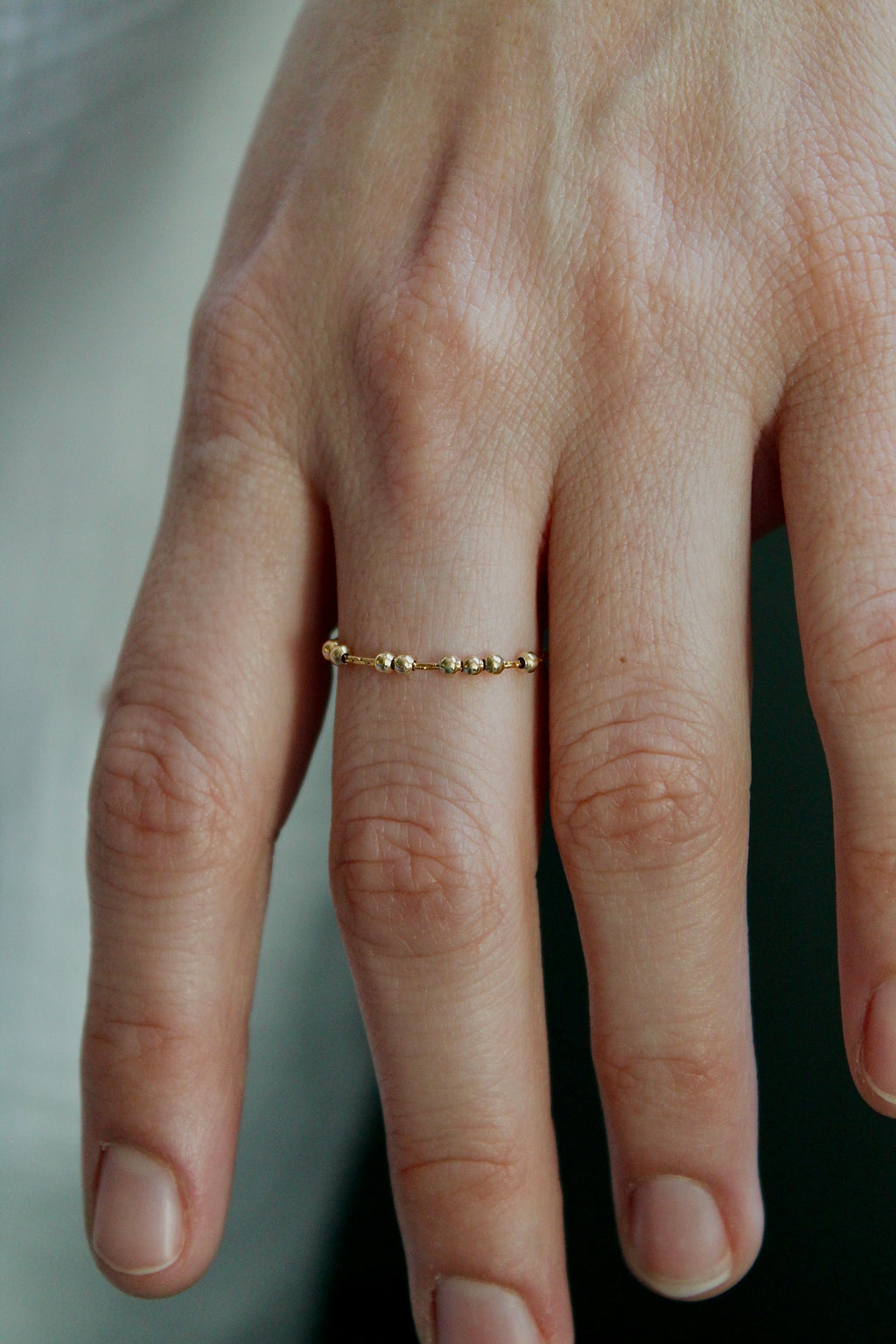 Close-up of a hand wearing a gold fidget spinner ring on a neutral background