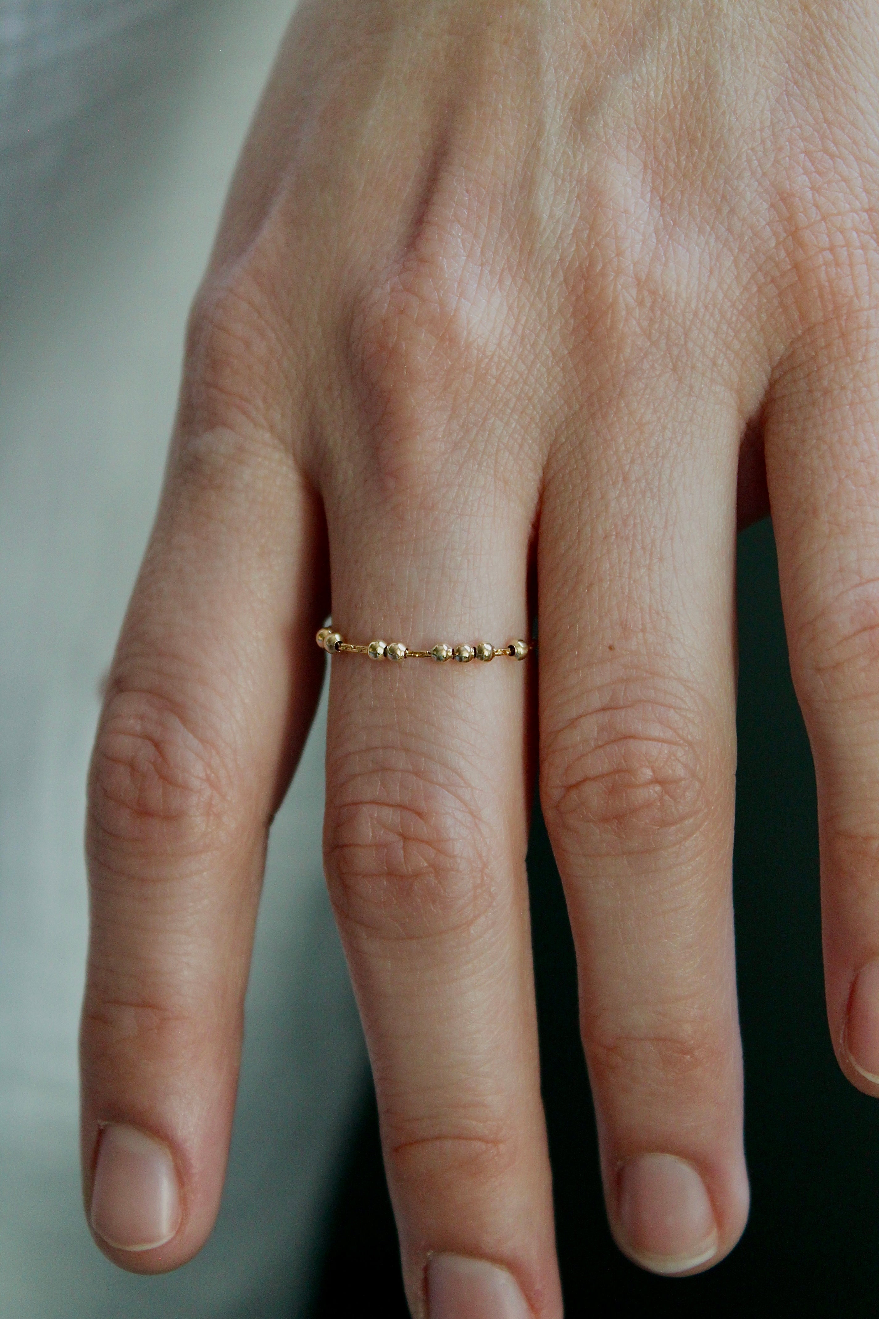 Close-up of a hand wearing a gold fidget spinner ring on a neutral background
