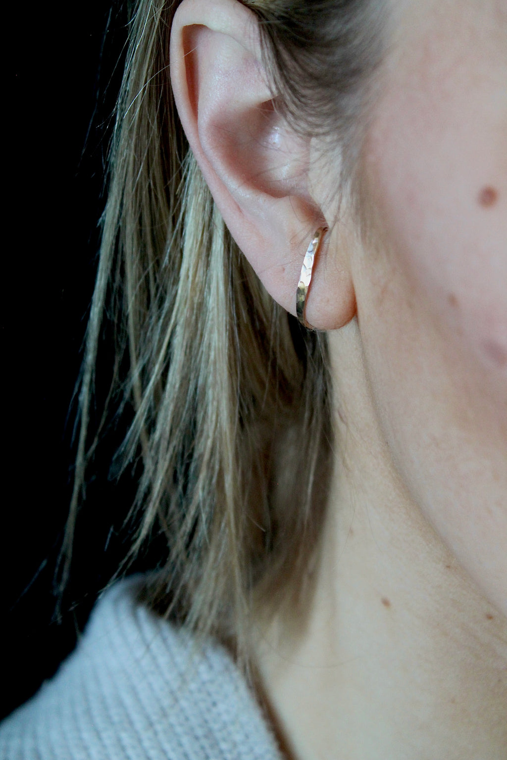 Close-up of an ear wearing a gold earring with a black background