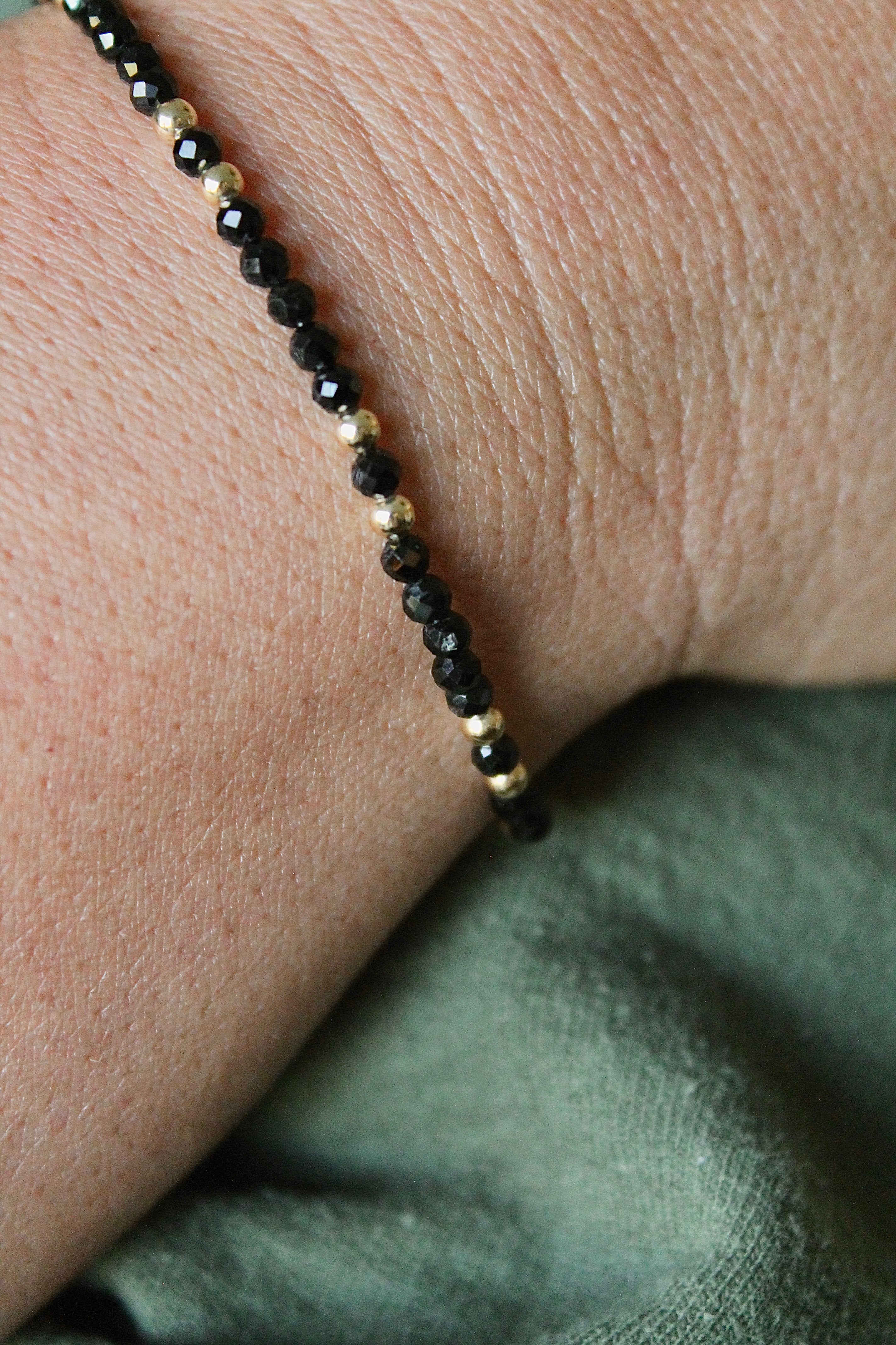 close-up of black and gold beaded bracelet on a wrist with green shirt background