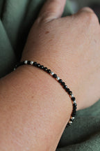 close-up of a black and silver beaded bracelet on a wrist with a green shirt background