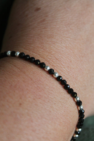 close-up of a black and silver beaded bracelet on a wrist with a green shirt background