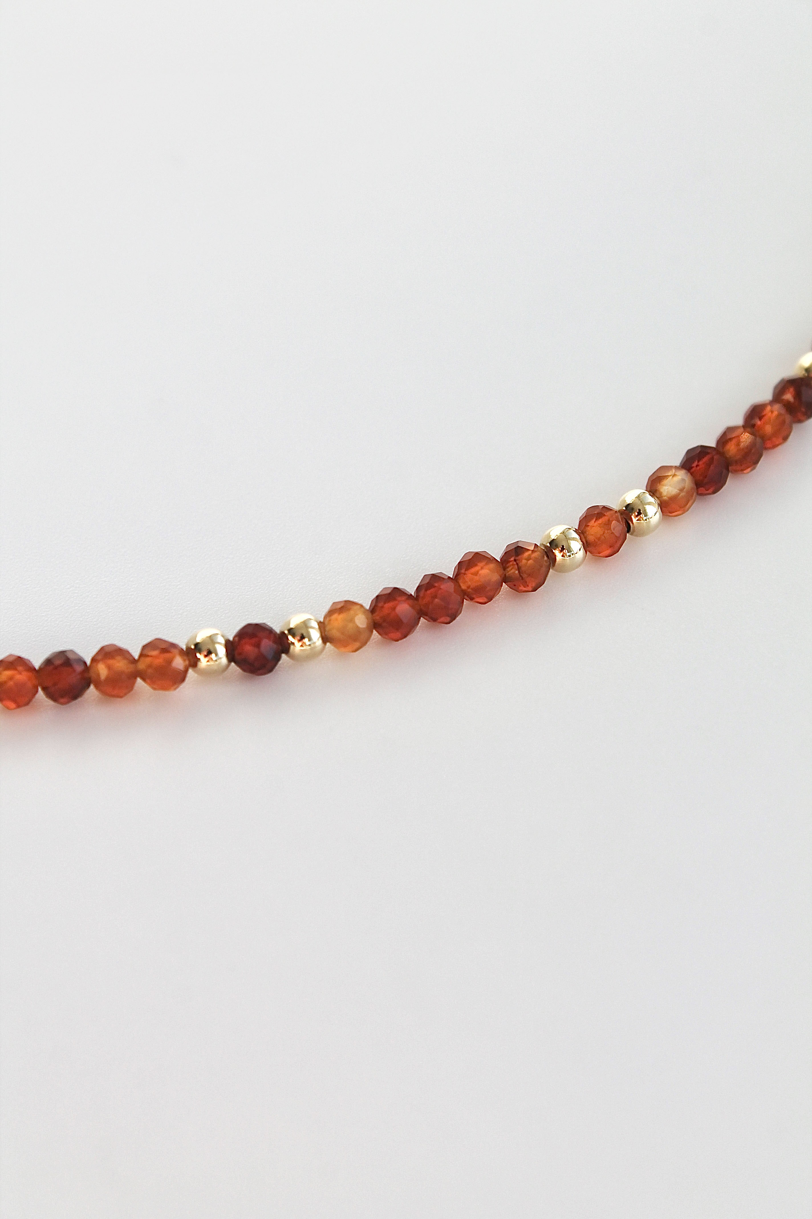 close-up of a carnelian and gold beaded bracelet on a white background
