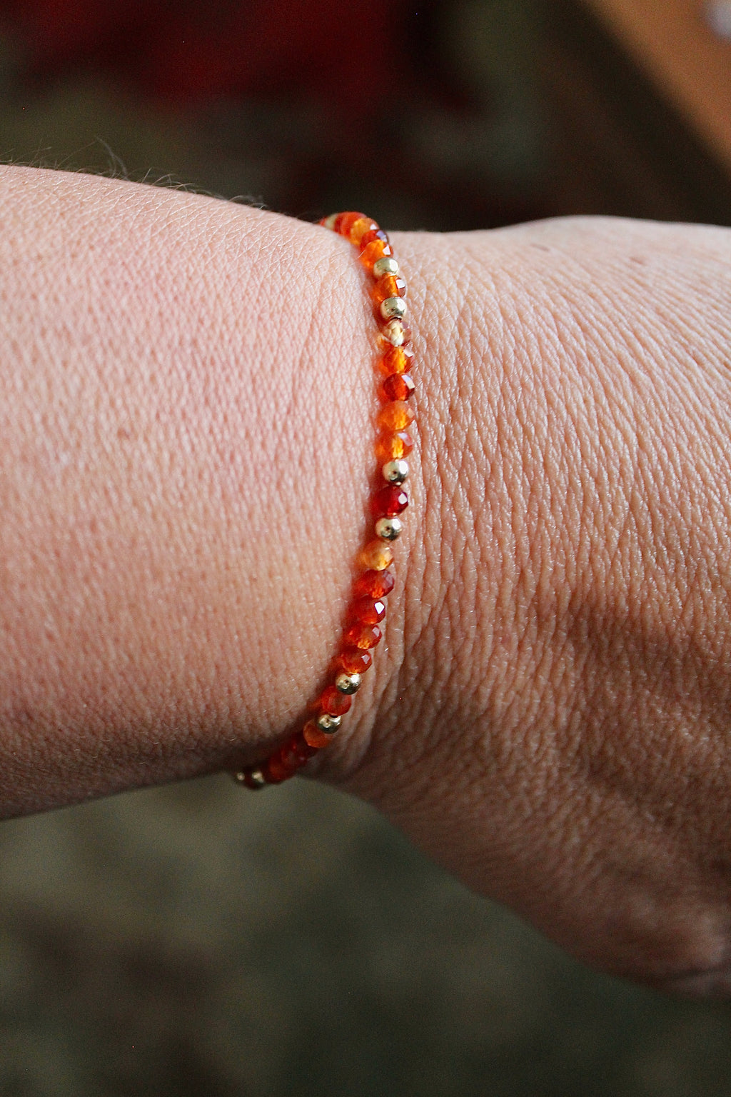 carnelian and gold beaded bracelet on a wrist with a muted green rug background