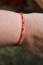 carnelian and gold beaded bracelet on a wrist with a muted green rug background