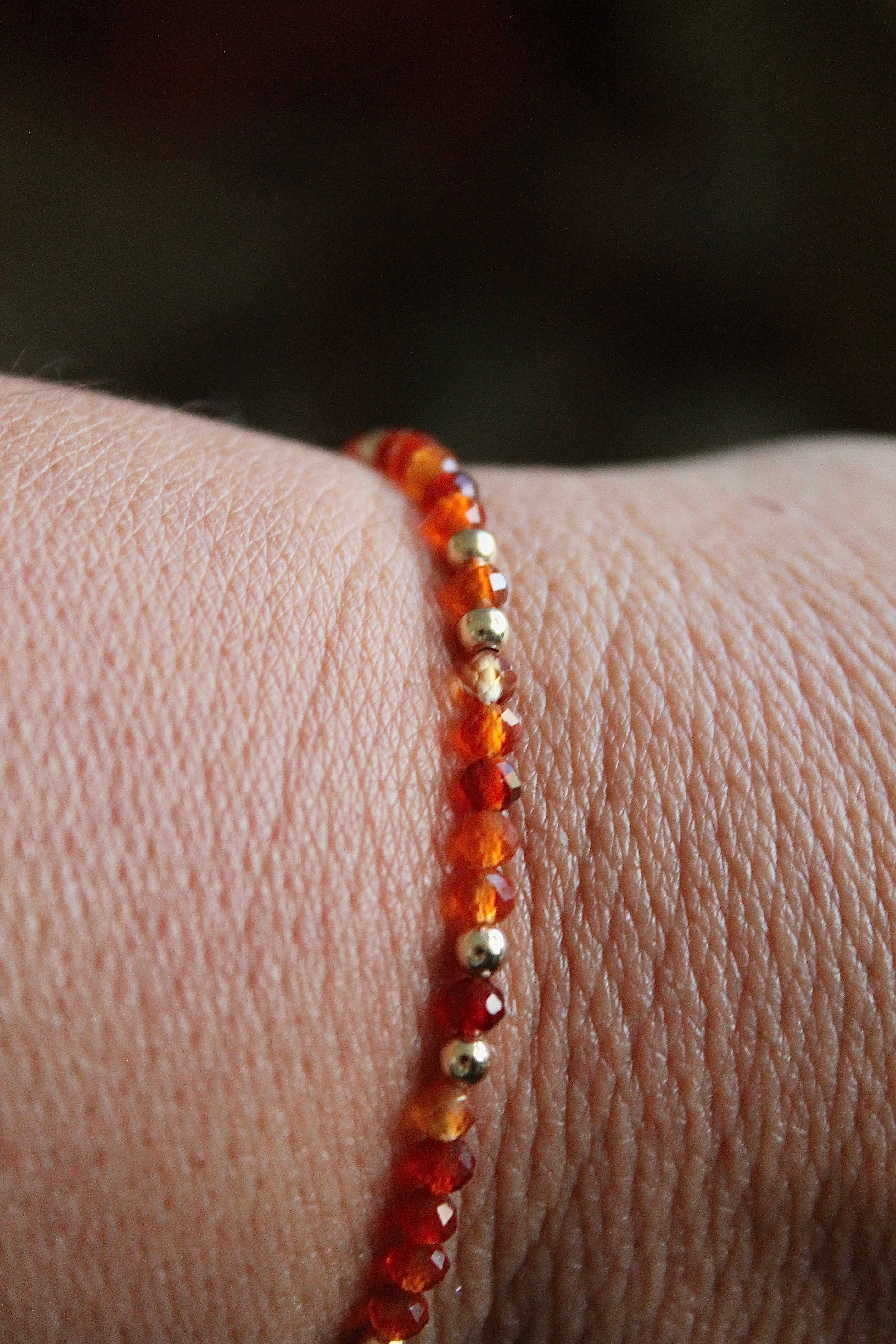Close-up of a wrist wearing a bracelet with carnelian and gold beads on a blurred background