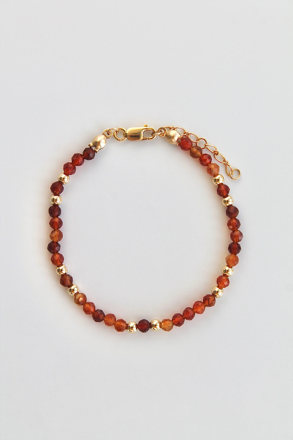 carnelian and gold beaded bracelet with gold clasp on a white background
