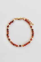 carnelian and gold beaded bracelet with gold clasp on a white background