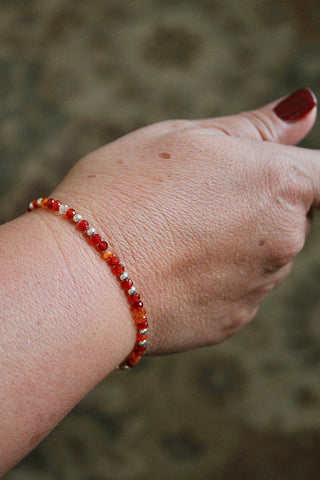 Hand wearing a carnelian and silver beaded bracelet against a blurred background
