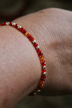 Close-up of a wrist wearing a carnelian and silver beaded bracelet against a blurred rug background