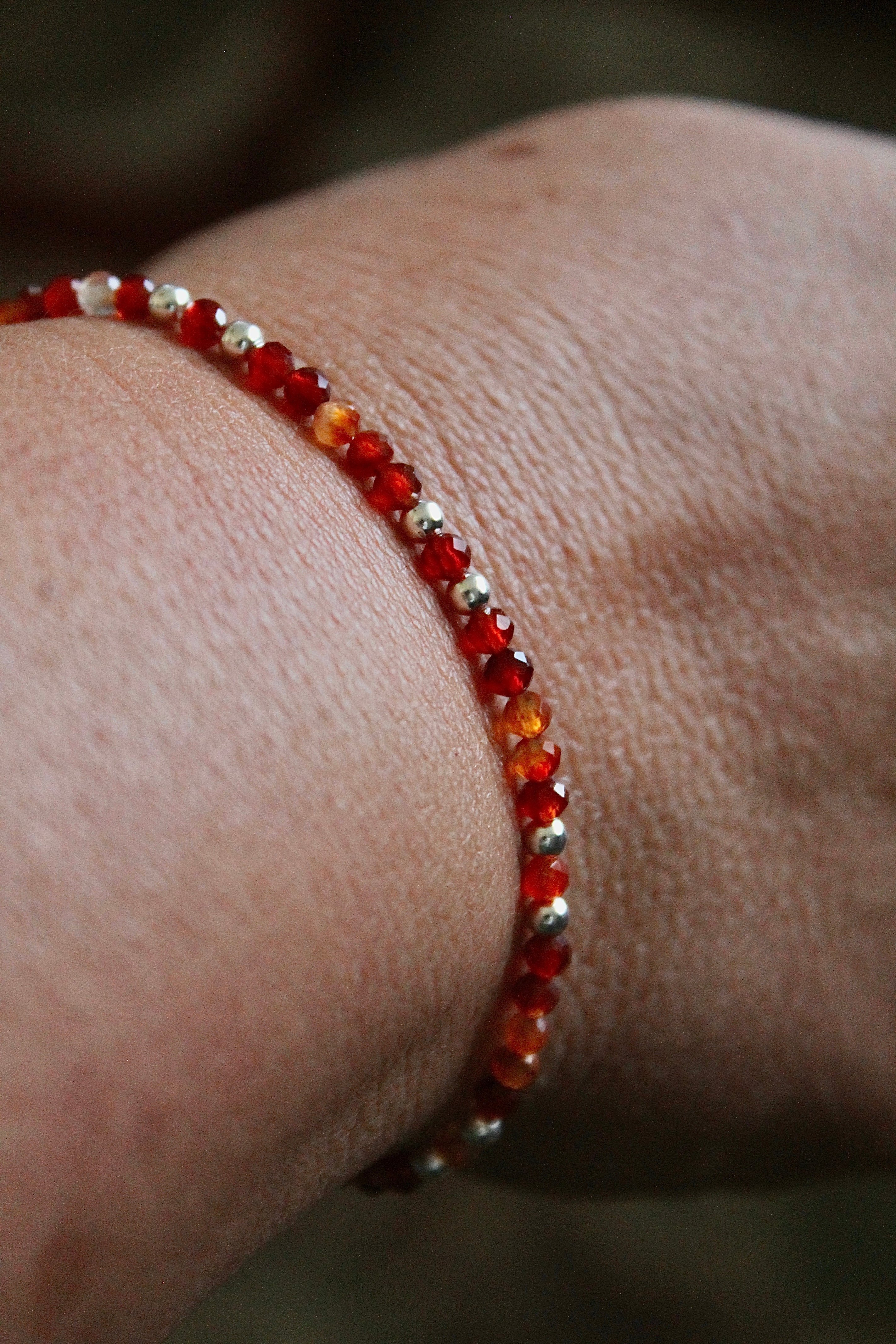 Close-up of a wrist wearing a carnelian and silver beaded bracelet against a blurred rug background