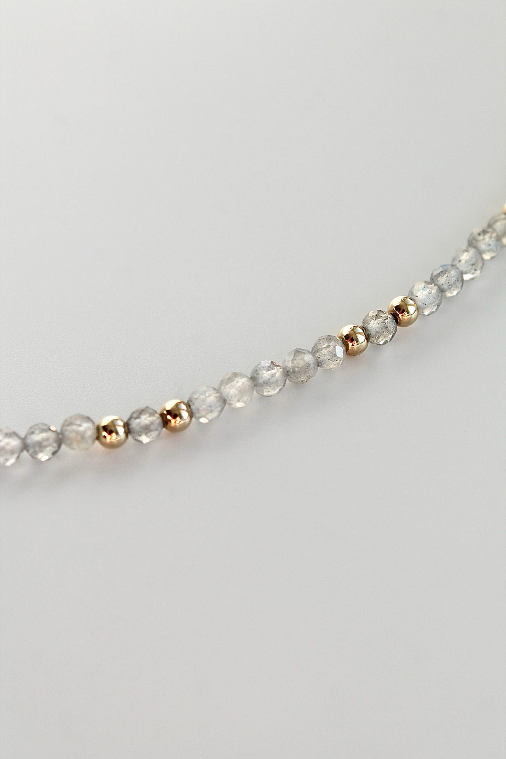 3mm round labradorite gemstone and gold bead bracelet close-up at an angle on a white background