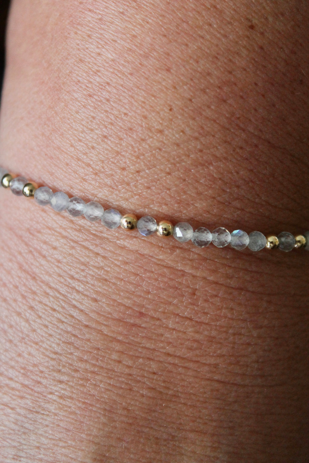 close-up of a labradorite gemstone and gold bead bracelet on a wrist