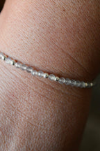 close-up of a labradorite gemstone and silver bead bracelet on a wrist with a blurred background